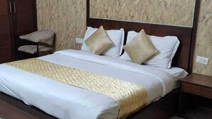 A neatly made bed with a wooden frame, white bedding, and two decorative pillows. - Hotel Green Lotus (Noida)