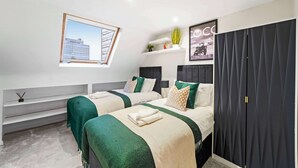 A modern bedroom with two beds, a skylight, a dark wardrobe, and a small shelf with plants. - Exclusive 2 Bedroom Flat near Barons Court! (Greater London)