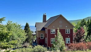 A two-story house with a balcony, surrounded by trees and a view of the water. - New owner!  10 minutes from the Massif with a view of the St Lawrence River! (Petite-Rivière-Saint-François)