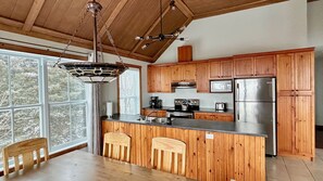A kitchen with wooden cabinets, a stainless steel refrigerator, a microwave, and a hanging light fixture.