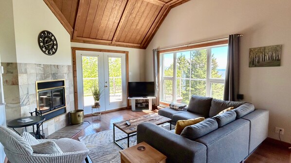 A living room with a fireplace, a sofa, a TV, and large windows.