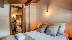 A bedroom with a large bed, a wooden ceiling, a wall-mounted light, and a door leading to a bathroom. - Apartment Mika - Alpes Agency - Central Chamonix - Sleeps 4-6 (Chamonix-Mont-Blanc)