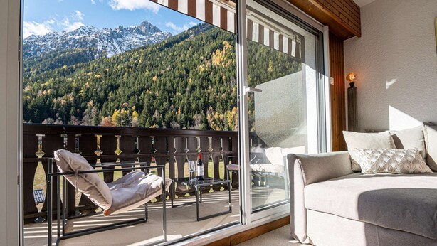 A balcony with a view of a mountainous landscape, a sofa, and a table with a bottle and glass. - Apartment Mika - Alpes Agency - Central Chamonix - Sleeps 4-6 (Chamonix-Mont-Blanc)