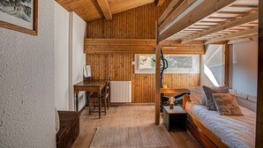 A cozy cabin interior with a wooden ceiling, a bed, a desk, and a window. - Apartment Mika - Alpes Agency - Central Chamonix - Sleeps 4-6 (Chamonix-Mont-Blanc)
