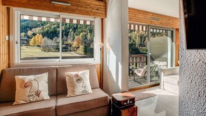 A cozy living room with a wooden ceiling, a sofa with decorative pillows, a large window with a scenic view, and a sliding glass door leading to an outdoor area. - Apartment Mika - Alpes Agency - Central Chamonix - Sleeps 4-6 (Chamonix-Mont-Blanc)