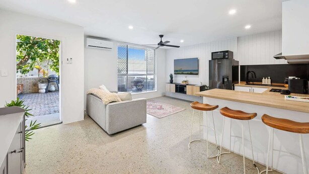 A modern kitchen with a bar area, a grey sofa, and a ceiling fan. - Spacious 1-Bed Apartment in Coolangatta (Coolangatta)