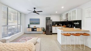 A modern kitchen with white cabinets, a black refrigerator, and a wooden countertop. There is a ceiling fan, a window with blinds, and a view of the outdoors. - Spacious 1-Bed Apartment in Coolangatta (Coolangatta)