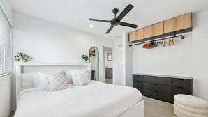 A modern bedroom with a white bed, a ceiling fan, a wooden wardrobe, and a hanging shoe rack. - Spacious 1-Bed Apartment in Coolangatta (Coolangatta)