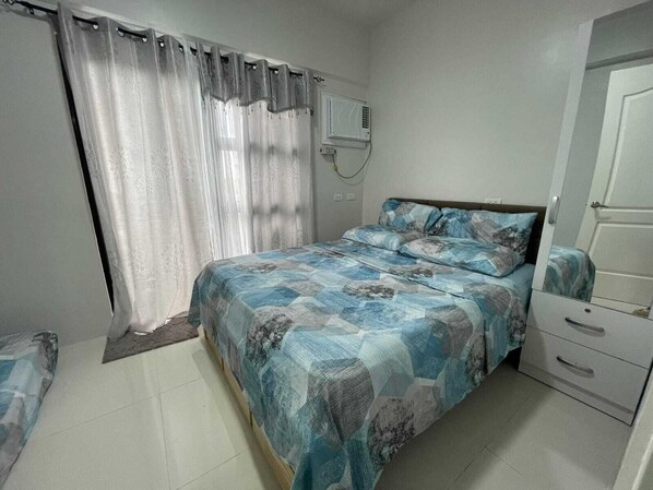 A bedroom with a bed, a dresser, a mirror, and a window with curtains. - Homestead OceanView (Dauis)