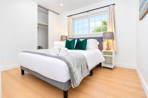 A modern bedroom with a bed, a nightstand, a lamp, a window with curtains, and a closet. - Spacious 4BR Home Mins to Santa Clara & Tech Campuses (San Jose)