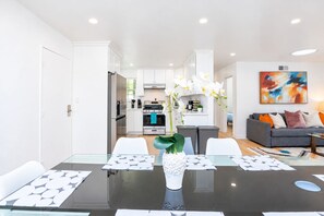 A modern kitchen with white cabinets, a dining table with a glass top, and a vase with flowers. - Spacious 4BR Home Mins to Santa Clara & Tech Campuses (San Jose)