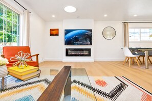 A modern living room with a fireplace, a flat-screen TV, and a dining area with a table and chairs. - Spacious 4BR Home Mins to Santa Clara & Tech Campuses (San Jose)