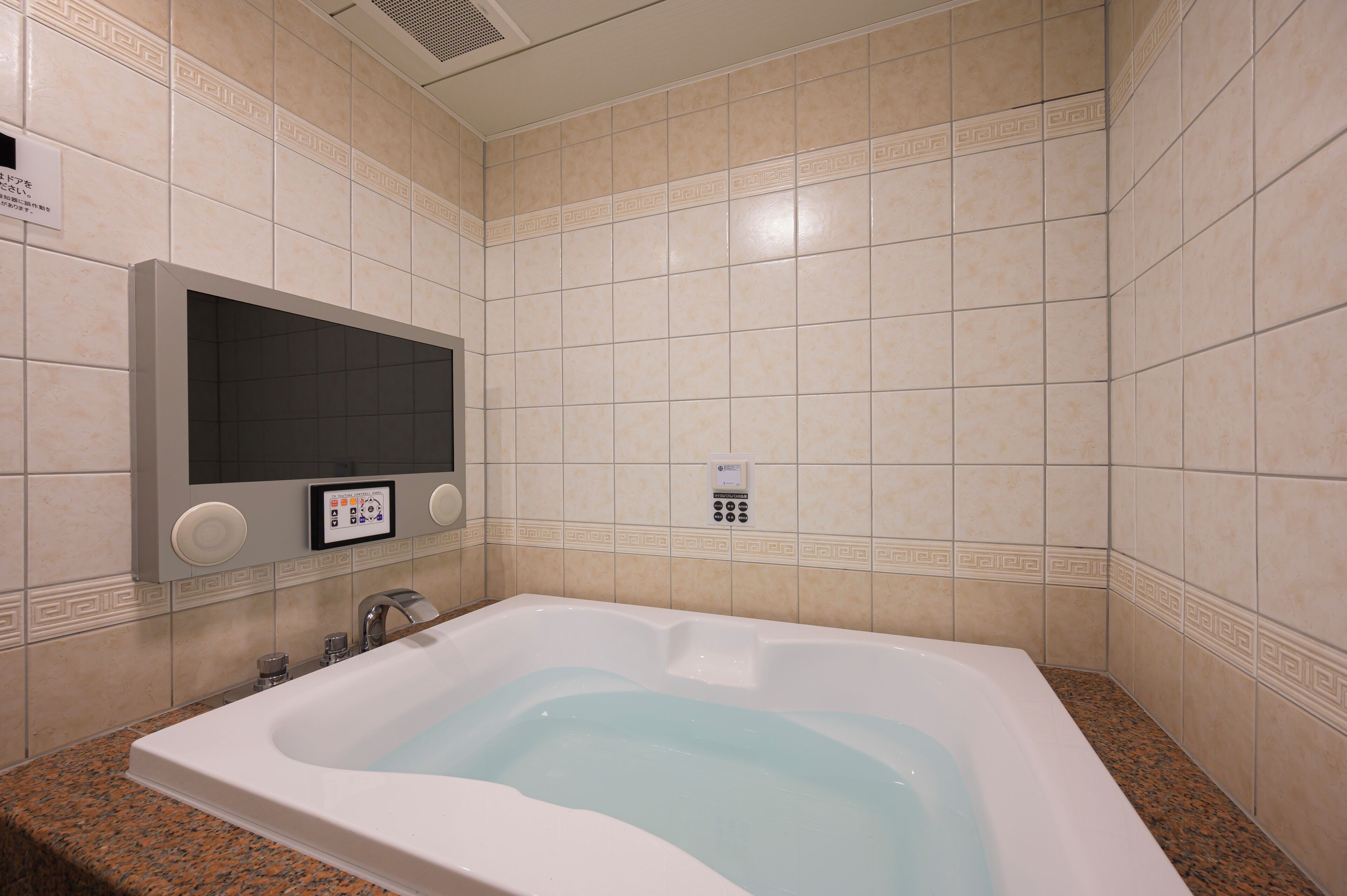 Ein Badezimmer mit einer großen Badewanne, einer wandmontierten Bedienkonsole und einer mit einem dekorativen Muster versehenen Fliesenwand.