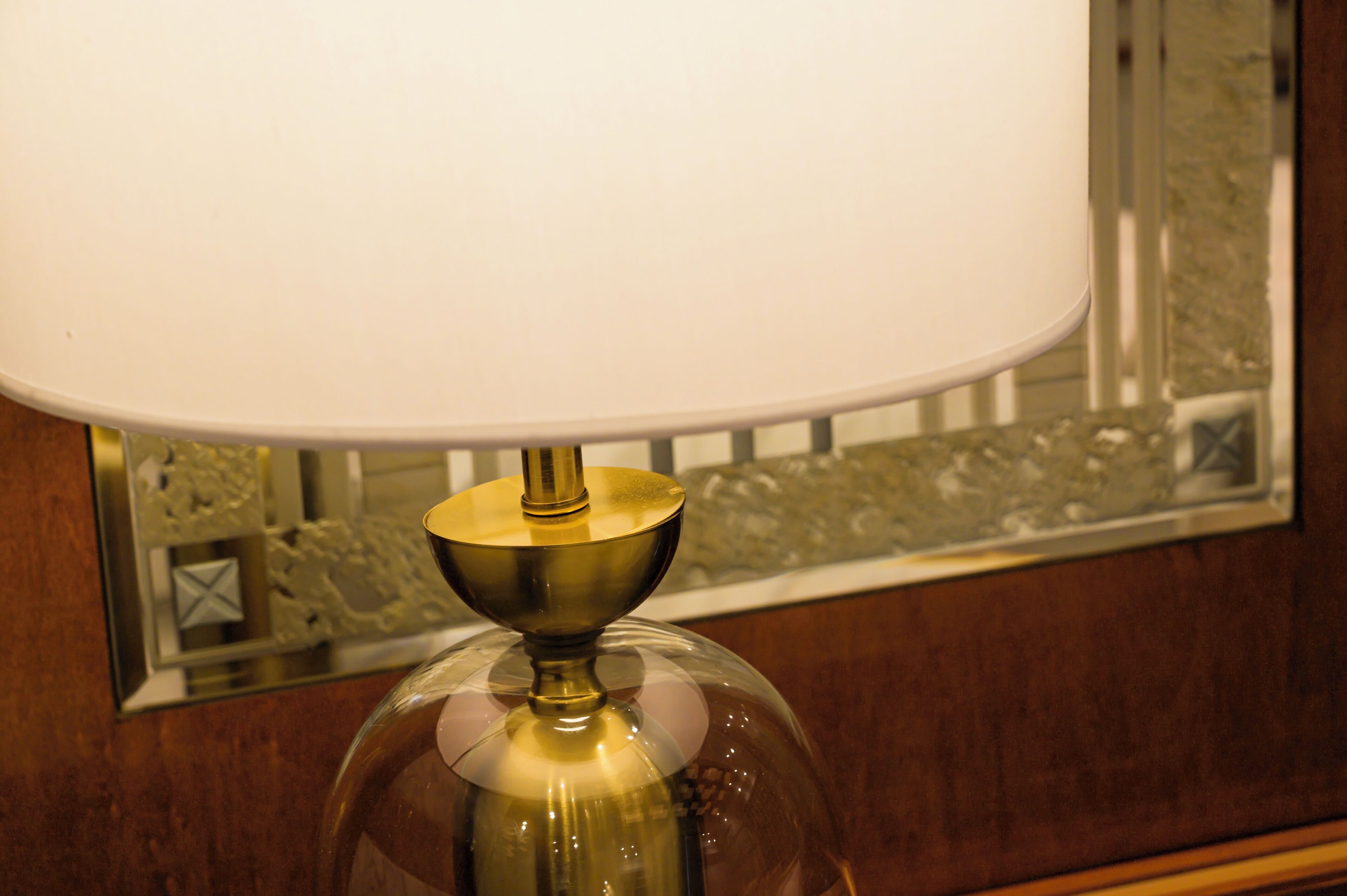 A table lamp with a clear glass shade and a brass base, positioned in front of a mirror with a decorative frame.
