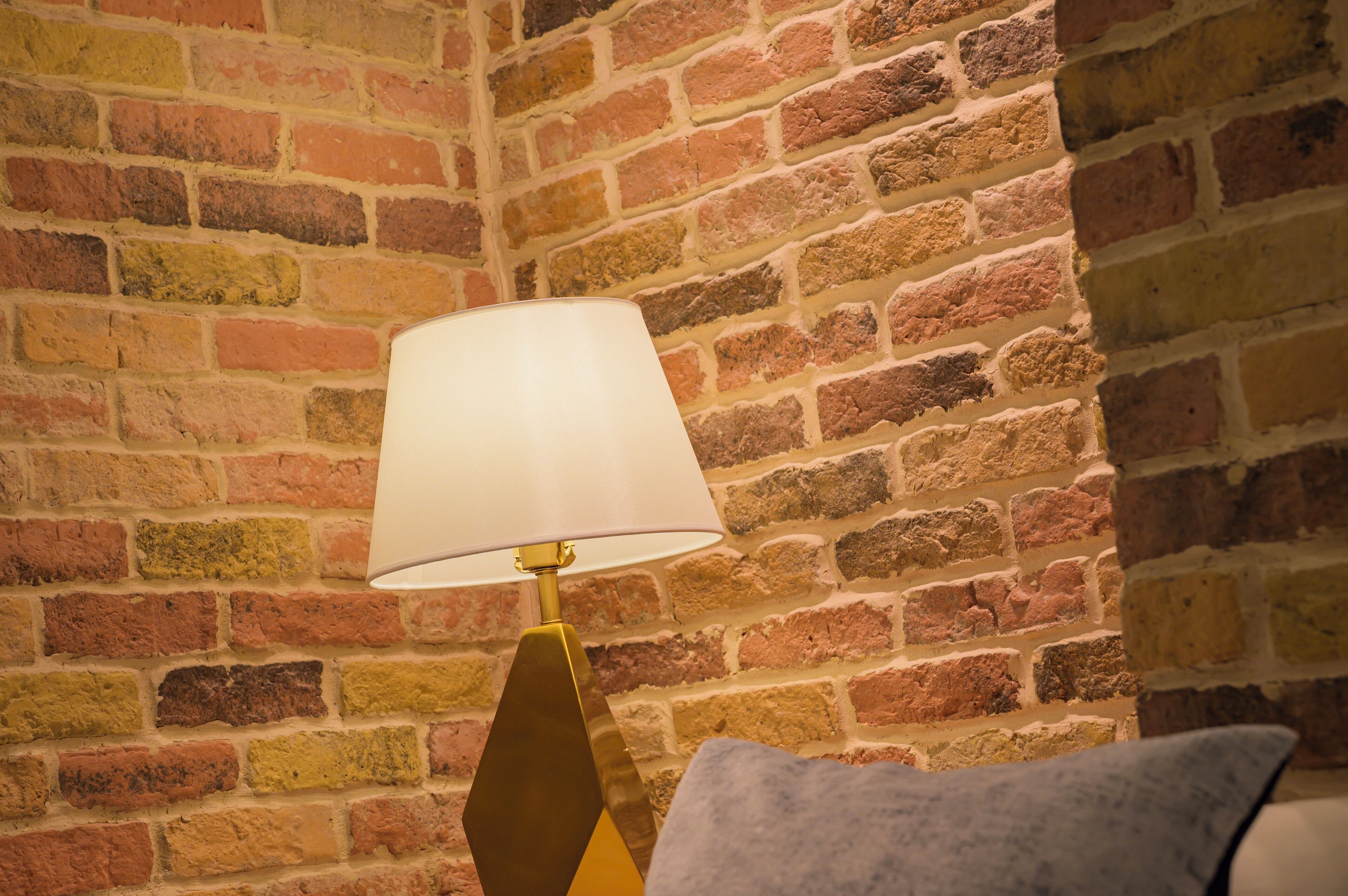Una habitación con pared de ladrillo y lámpara con pantalla blanca.
