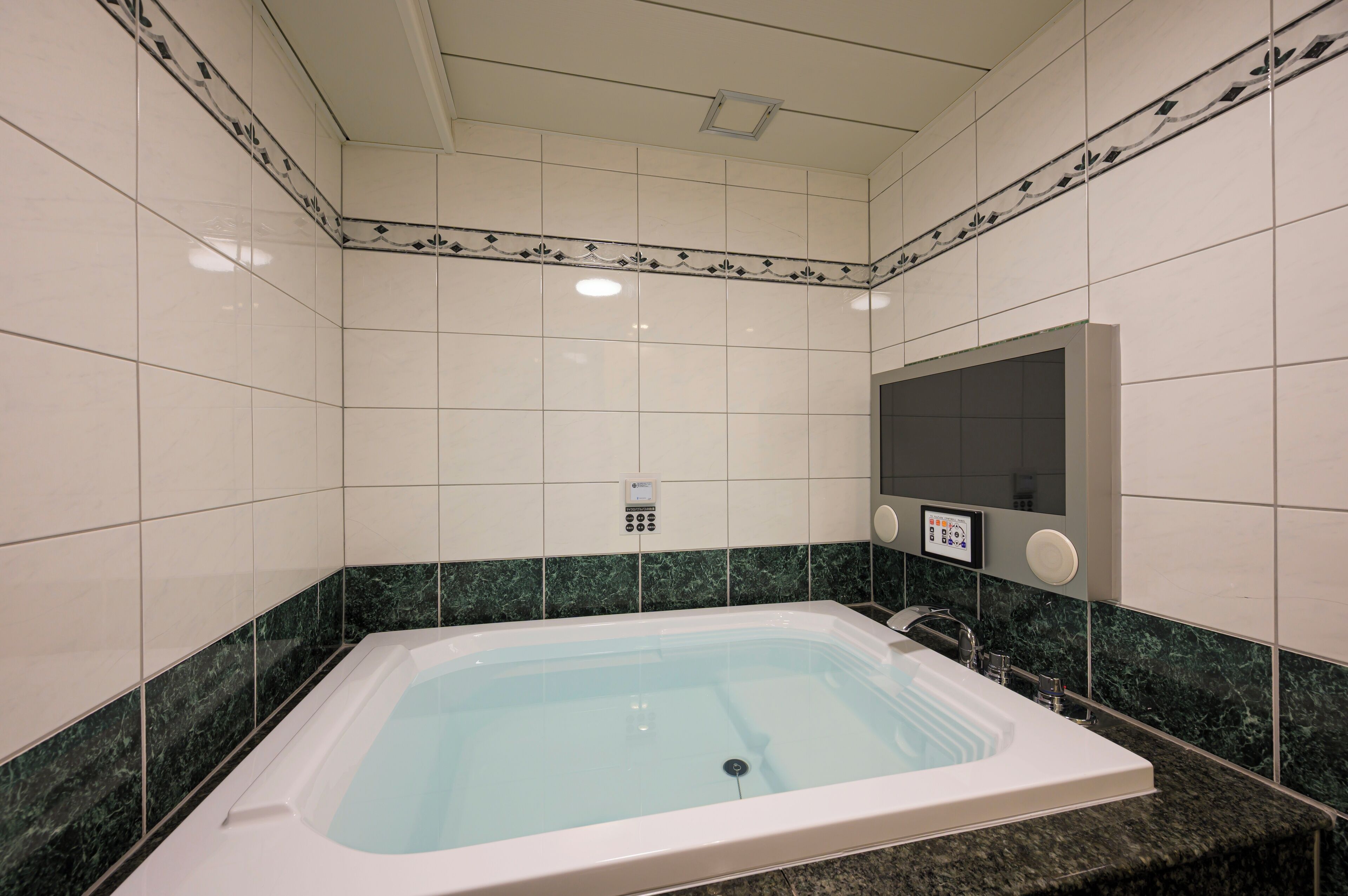 A modern bathroom with a large bathtub, a wall-mounted control panel, and a mirror.