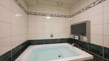 A modern bathroom with a large bathtub, a wall-mounted control panel, and a mirror.