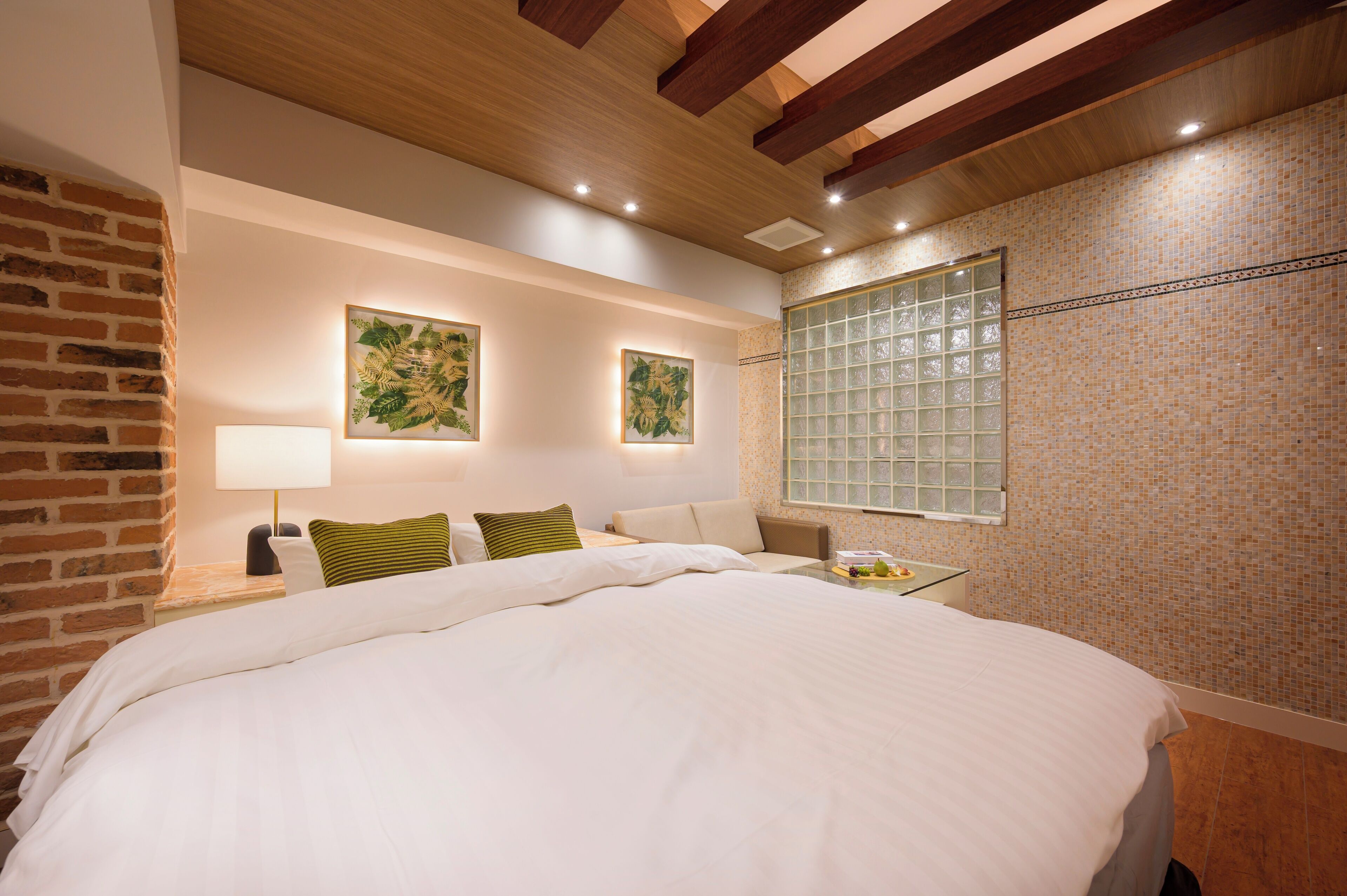 Une chambre d’hôtel moderne avec un grand lit, un mur en briques et deux reproductions botaniques encadrées accrochées au mur.