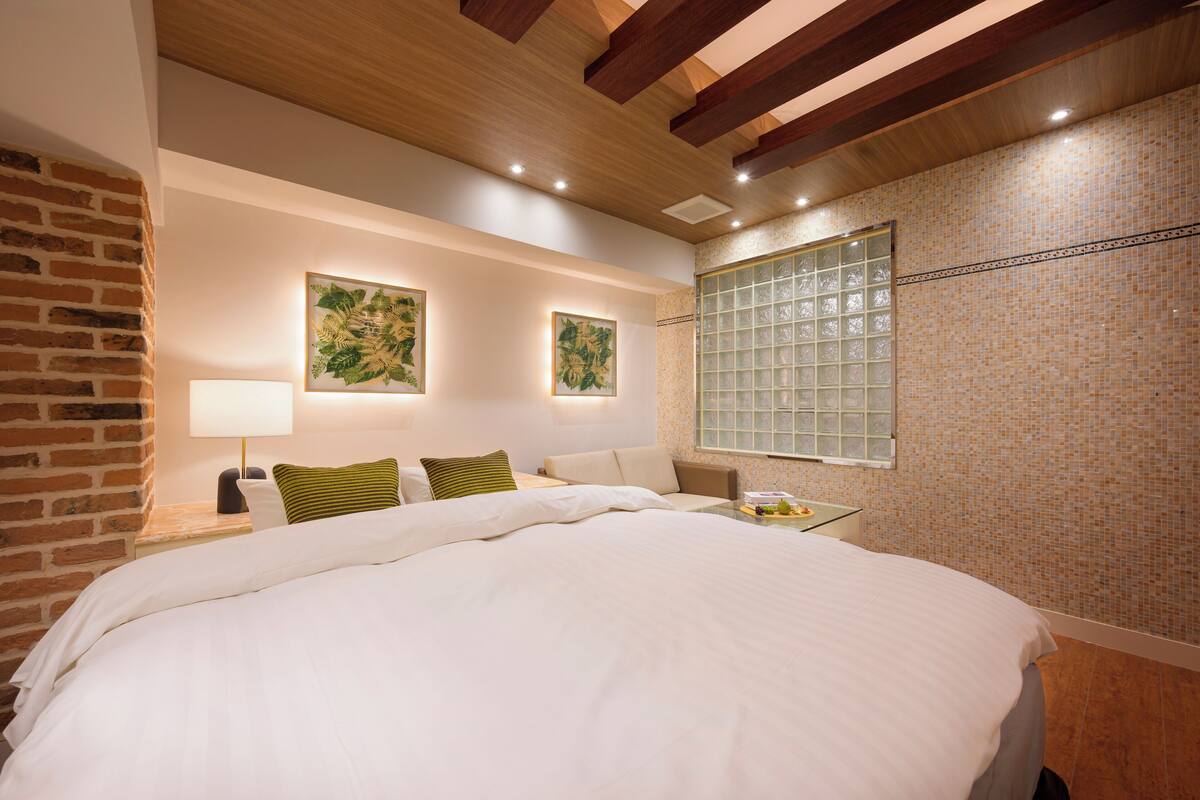 A modern hotel room with a large bed, a brick wall, and two framed botanical prints on the wall.