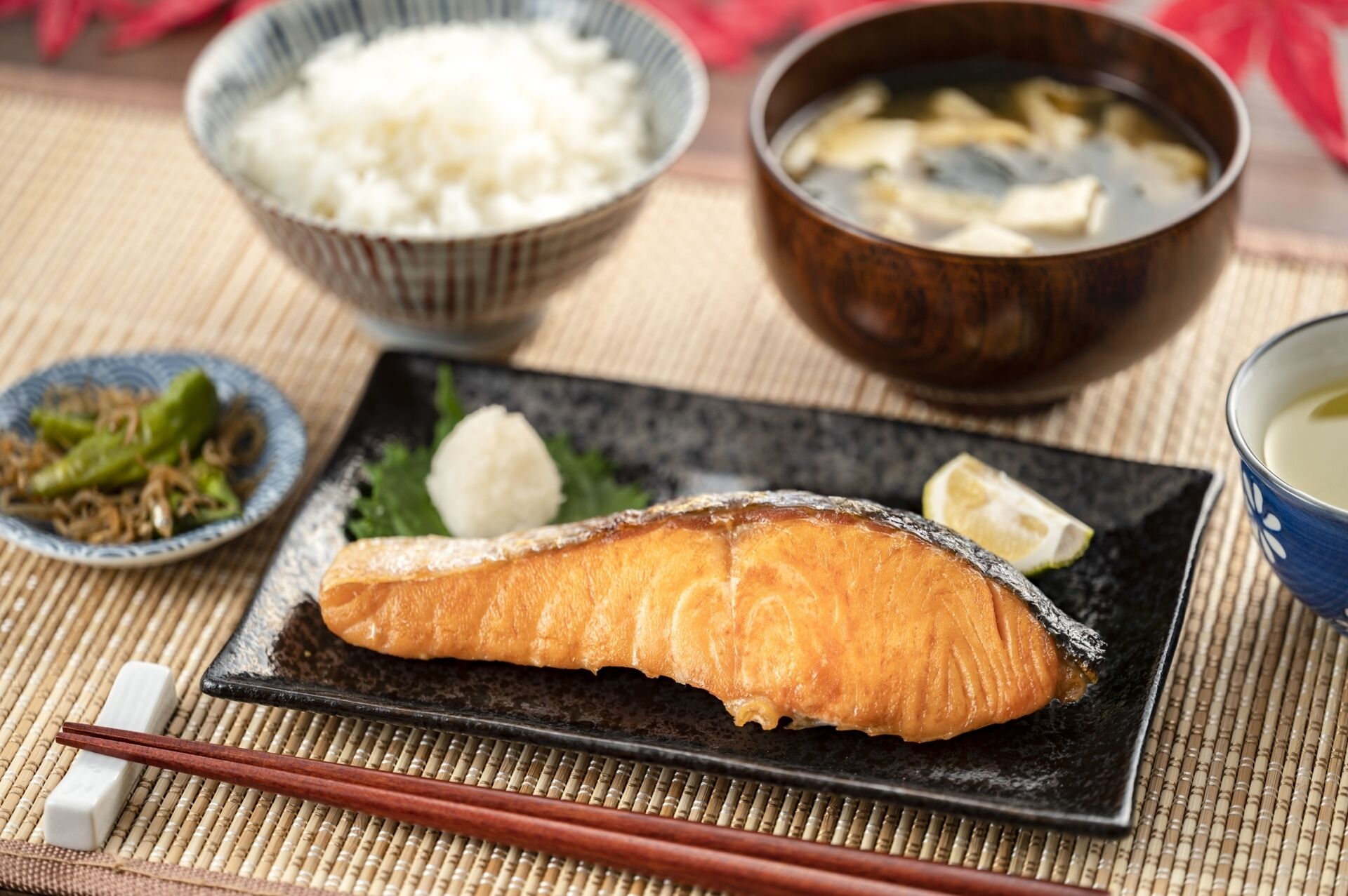 A plate with a piece of salmon, a bowl of rice, a bowl of soup, and a small dish of pickled vegetables.