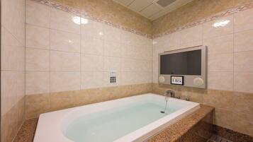 Ein modernes Badezimmer mit einer großen Badewanne, einer integrierten Toilette und einem an der Wand befestigten Fernseher.