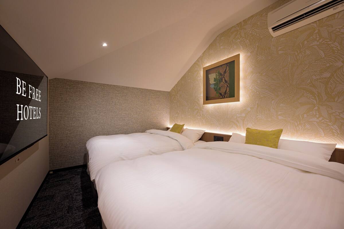A hotel room with two beds, a flat-screen TV, and a wall-mounted painting.