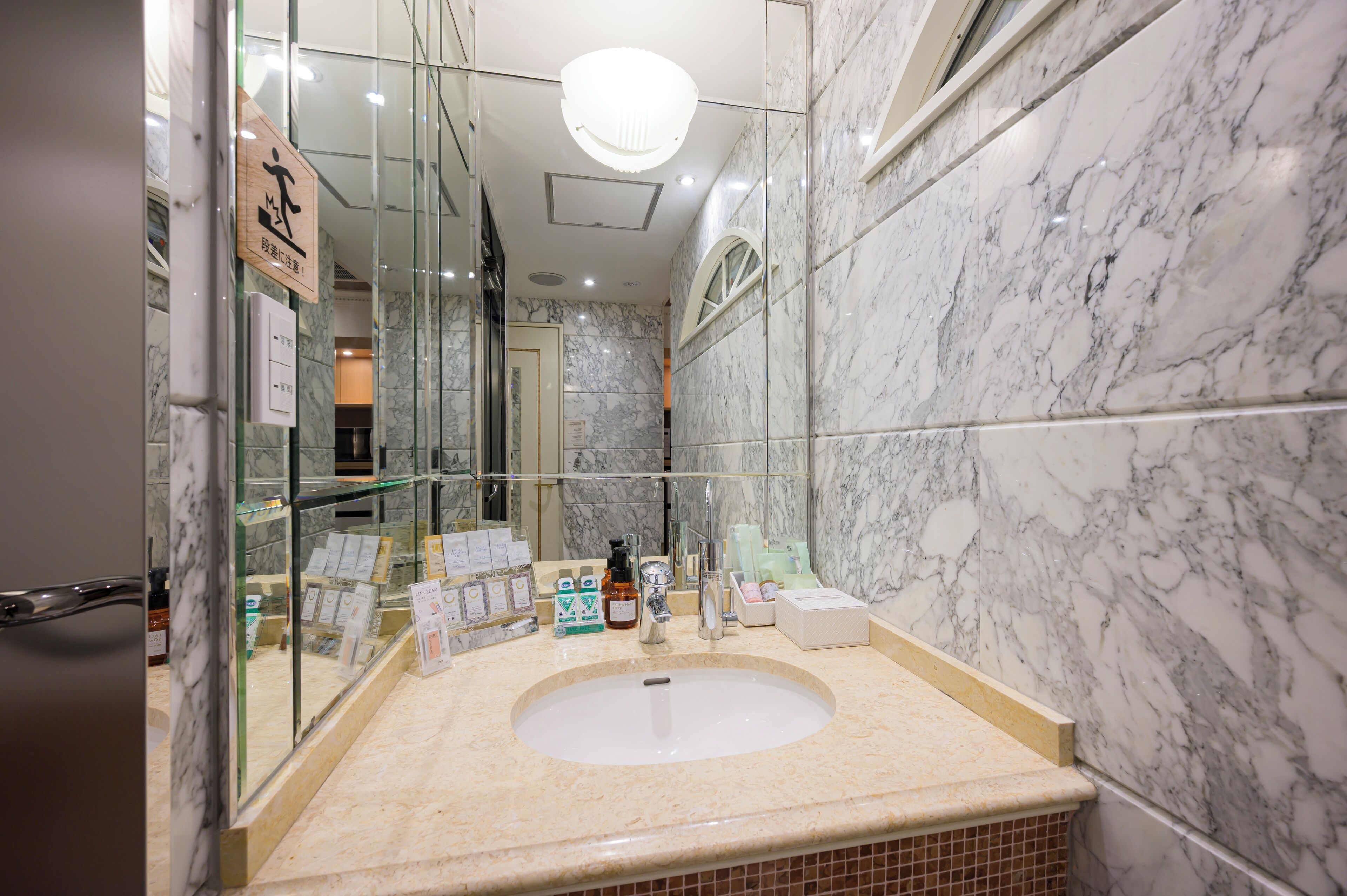 Un baño con lavamanos de mármol, vitrina de vidrio y un espejo.