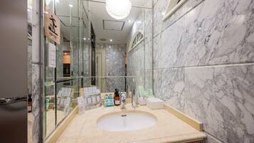 Un baño con lavamanos de mármol, vitrina de vidrio y un espejo.