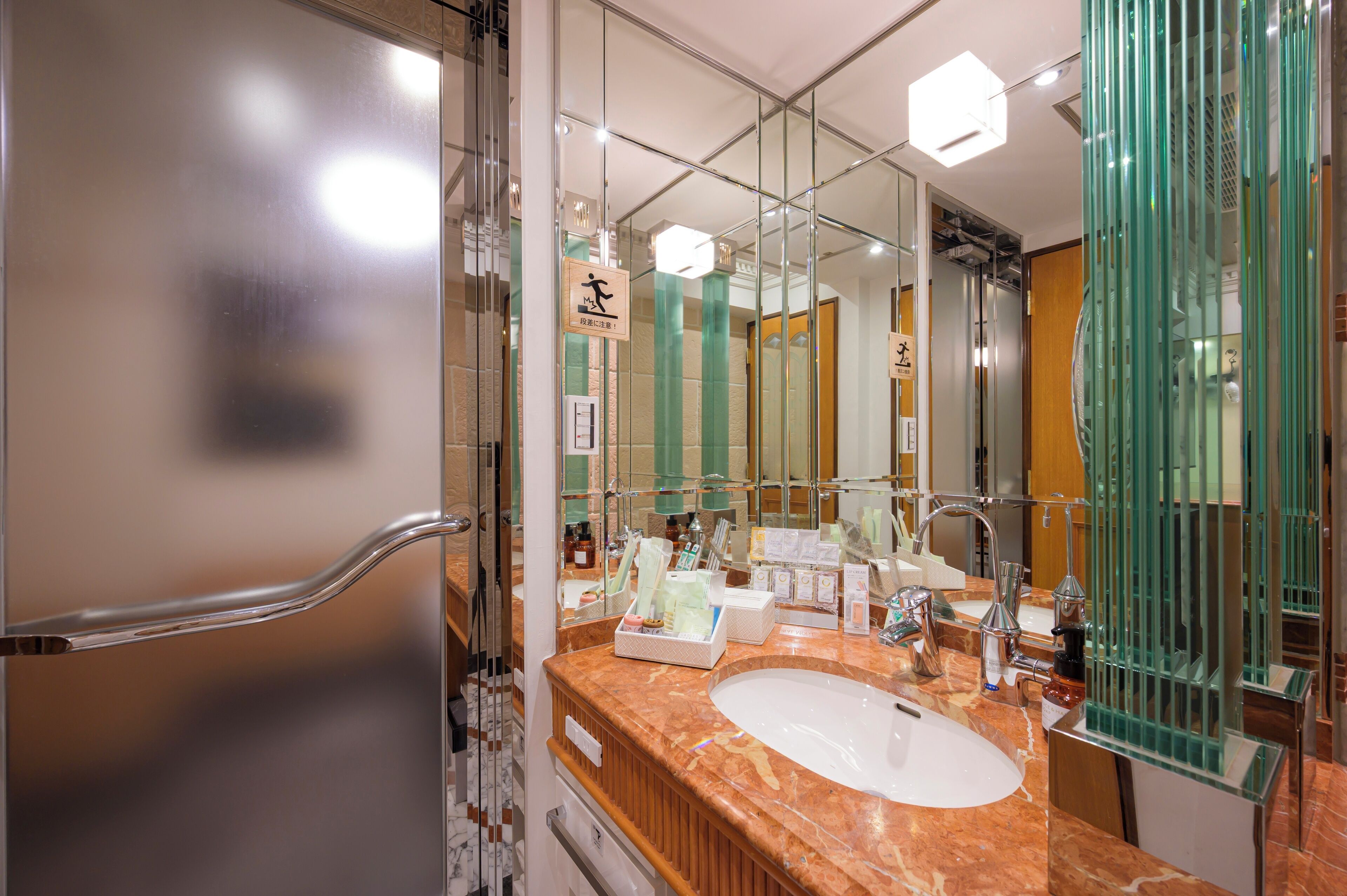 Un baño moderno con lavamanos de mármol, cabina de ducha de vidrio y un espejo grande que refleja el ambiente.