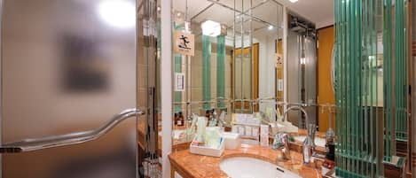 Un baño moderno con lavamanos de mármol, cabina de ducha de vidrio y un espejo grande que refleja el ambiente.