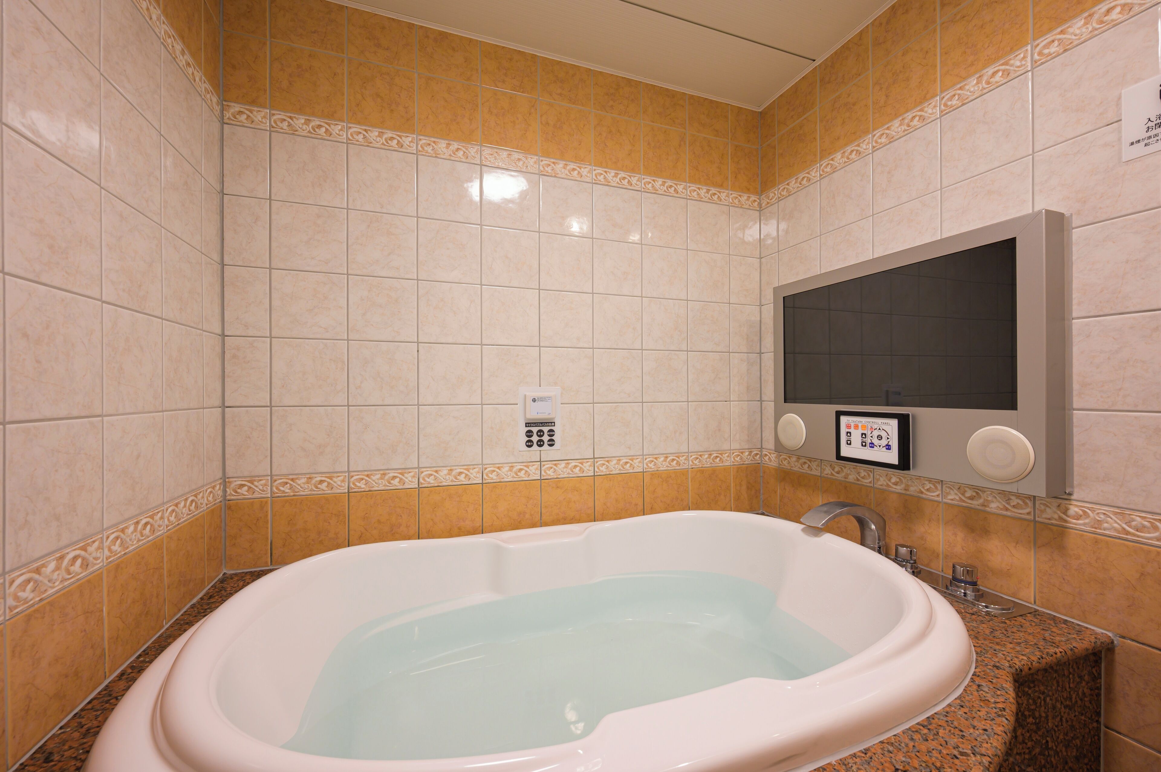 Un baño con una bañera grande, un televisor montado en la pared y un panel de control.