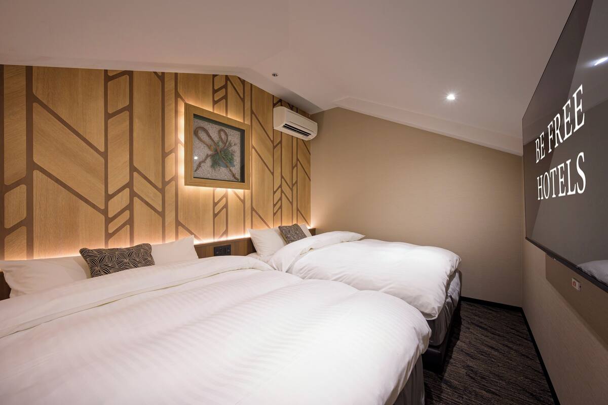 A hotel room with two beds, a wall-mounted air conditioner, and a sign that says "BE FREE HOTELS".