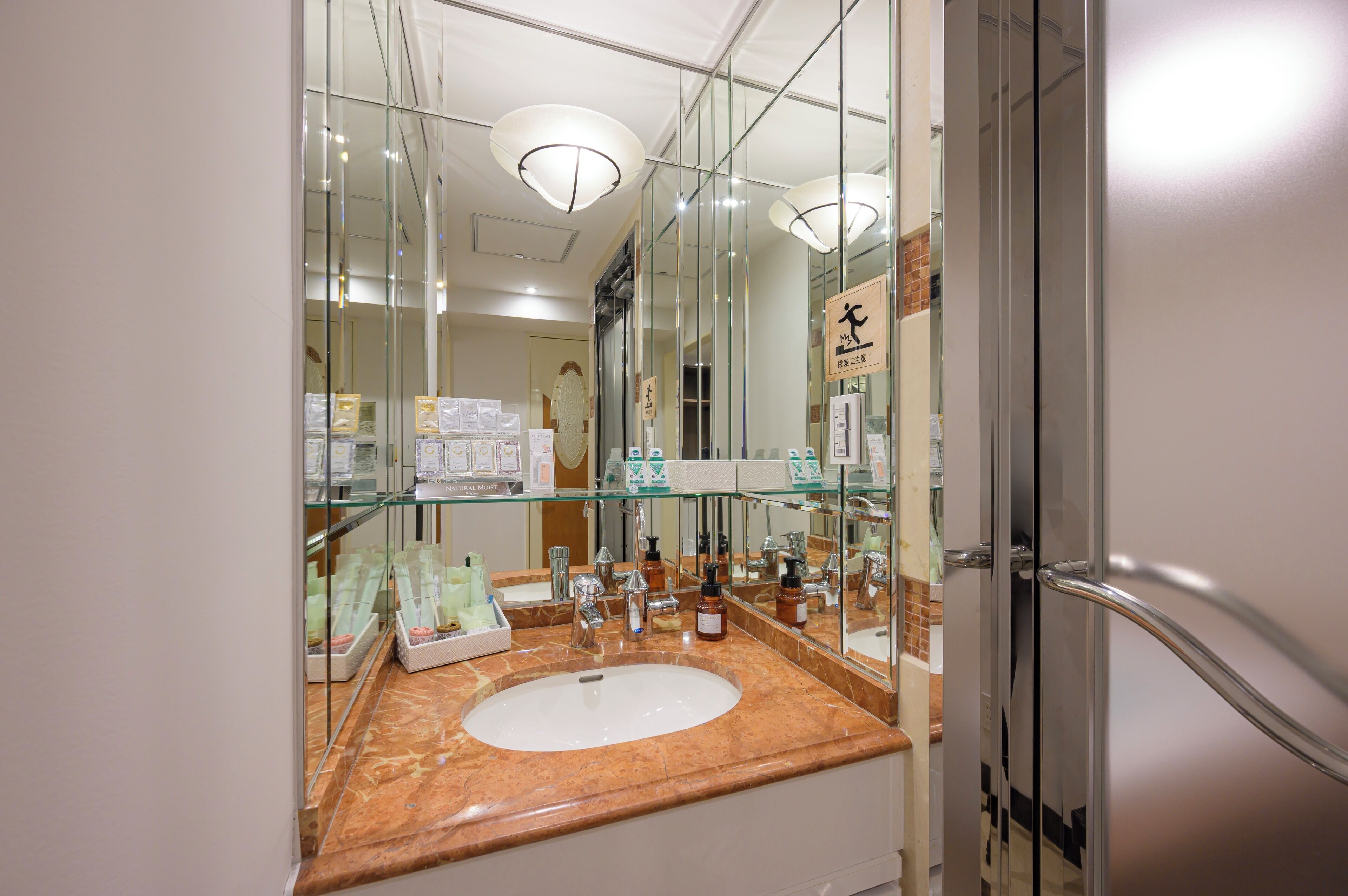 Een badkamer met een glazen wastafel, meerdere spiegels en een zichtbaar toilet.