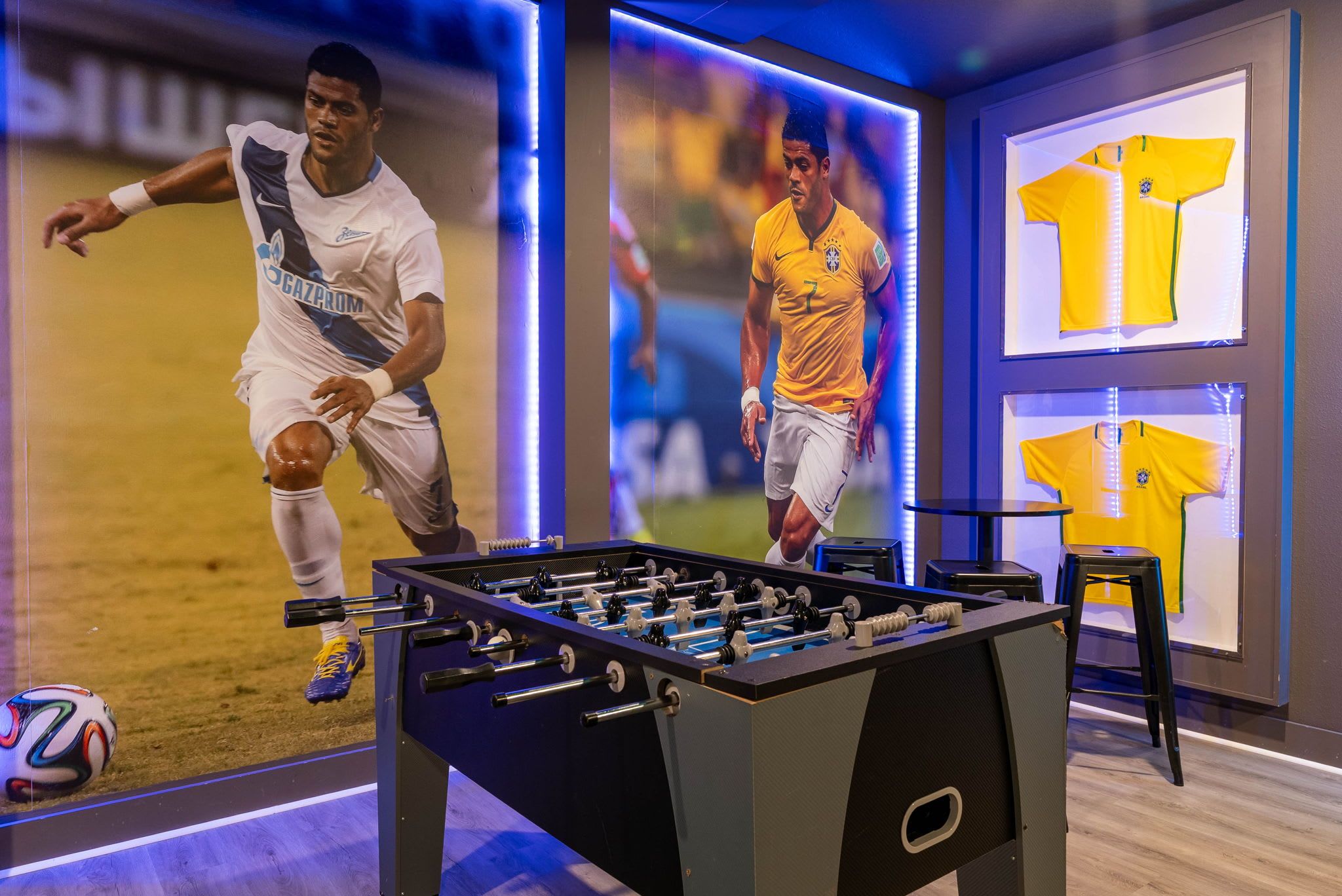 Uma mesa de futebol de mesa em um quarto com itens de colecionador de esportes, incluindo camisas de futebol e uma bola de futebol.
