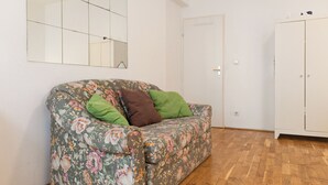Een kamer met een bank met bloemendesign, een spiegel, een garderobe en een houten vloer.