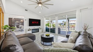 Ein modernes Wohnzimmer mit einem großen Flachbildfernseher, einem Deckenventilator und Blick ins Freie durch große Schiebeglastüren.