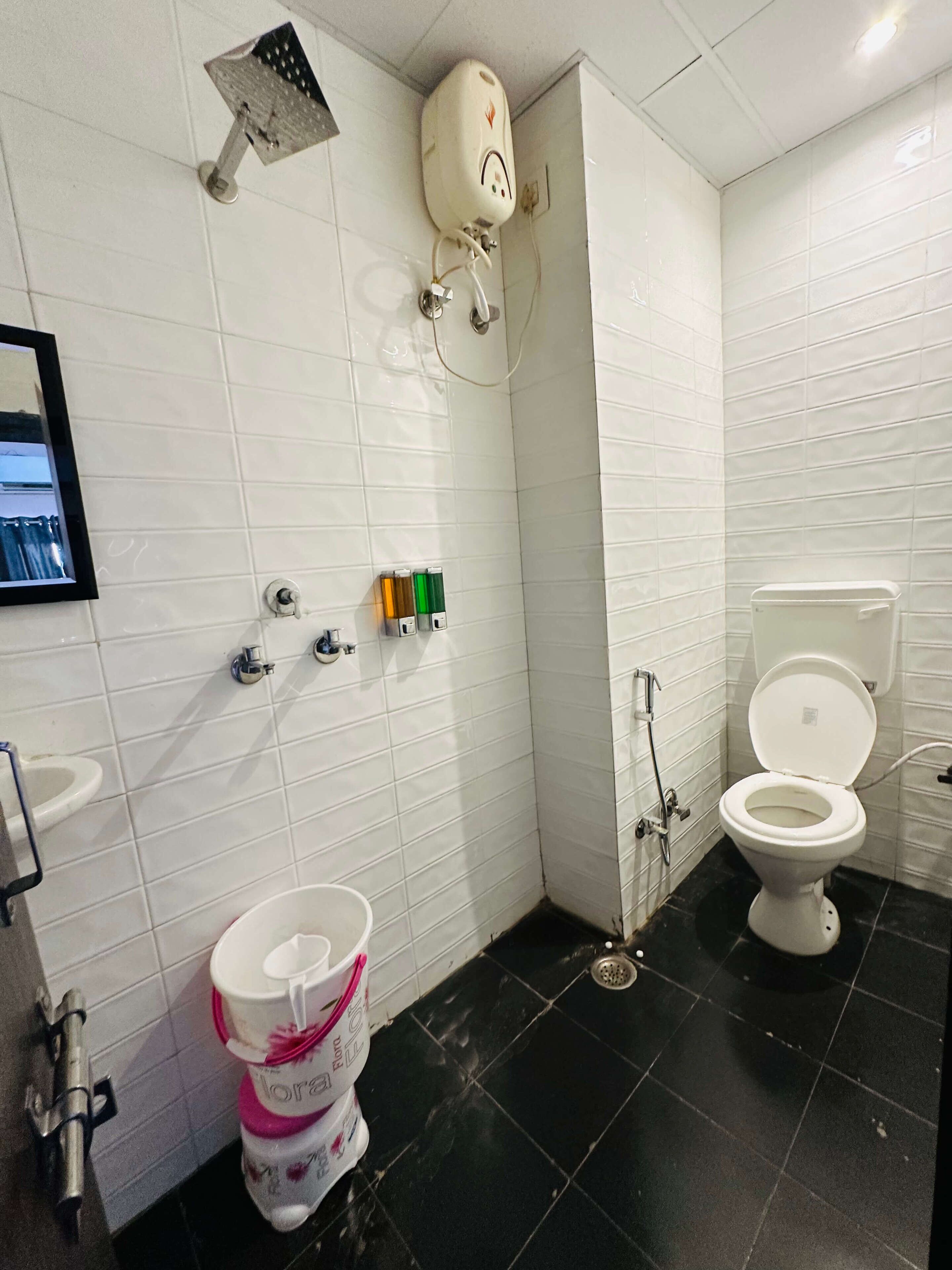 A bathroom with a toilet, sink, and shower. There are soap dispensers and a toilet paper holder on the wall.