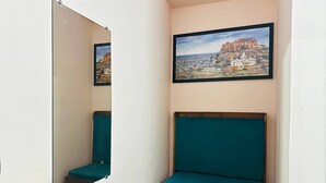 Una habitación estrecha con un banco azul verdoso, una mesa de madera y un cuadro enmarcado de un edificio histórico en la pared.