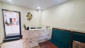 Zona de recepción con mostrador de mármol, una mesa de madera y un sofá verde.