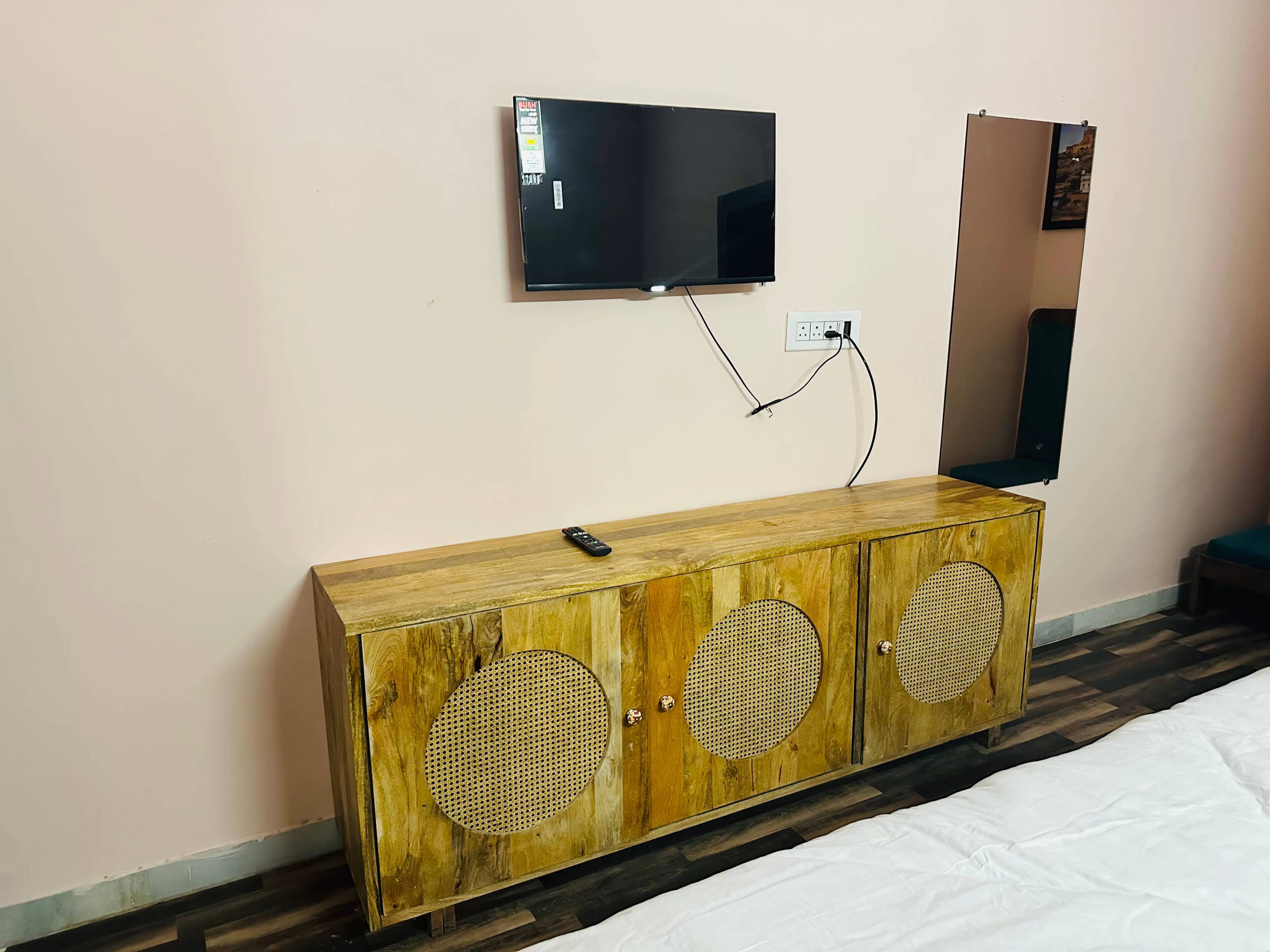 A wooden cabinet with two circular speakers, a television mounted on the wall, and a remote control on the cabinet.