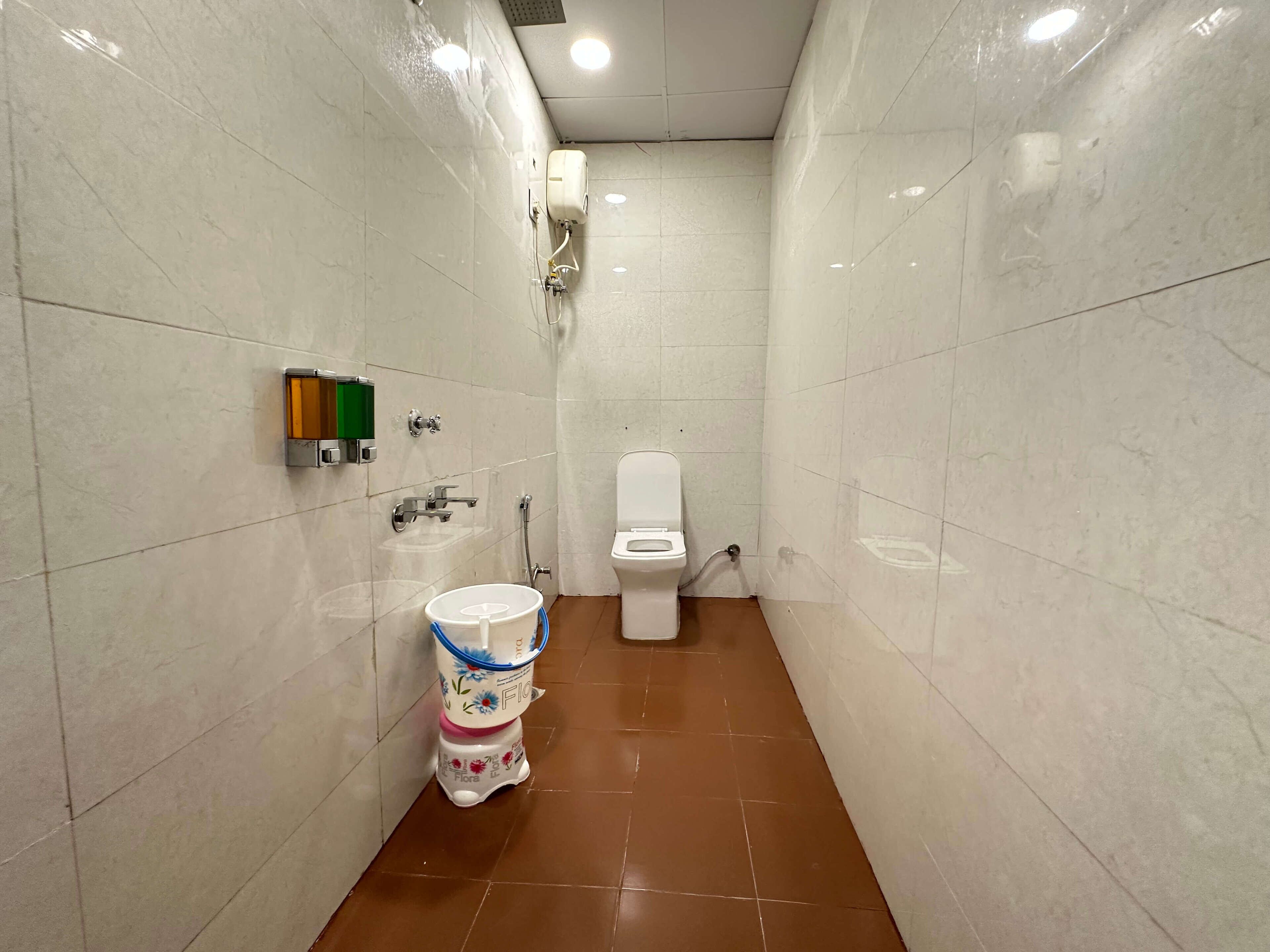 A small, tiled bathroom with a toilet, a wall-mounted hand dryer, and a trash bin.