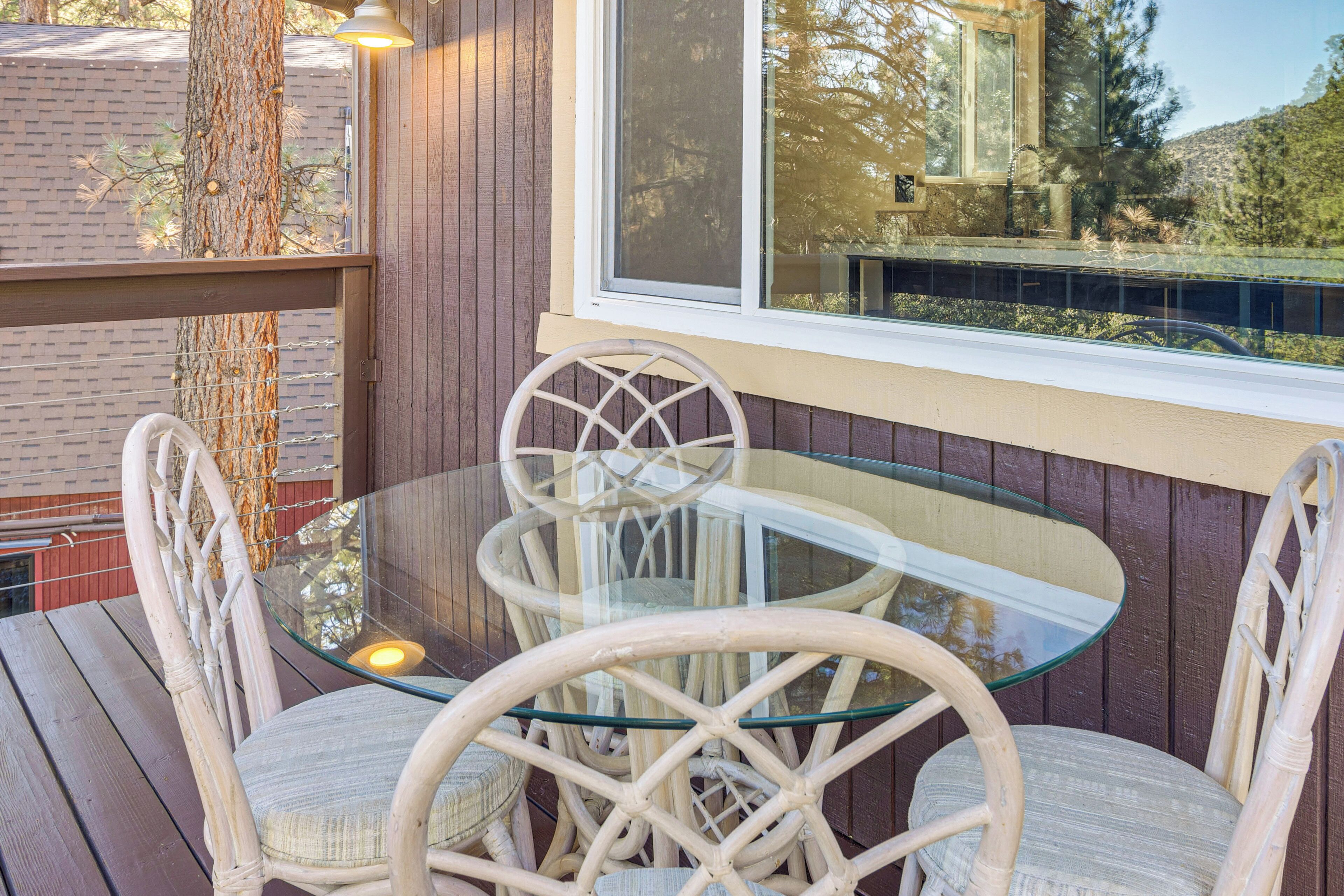 Een tafel met glazen blad en rieten stoelen op een houten terras.