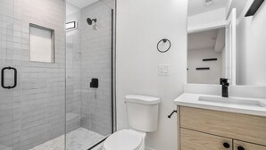 Ein modernes Badezimmer mit Duschkabine aus Glas, einer weißen Toilette und einem Holzausleger mit Spiegel.