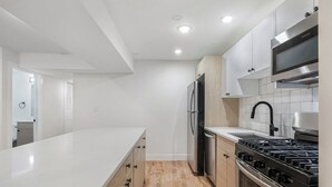 Eine moderne Küche mit weißen Schränken, einem Edelstahl-Kühlschrank, einem Gasherd und einer Mikrowelle.