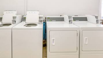 A row of white, industrial-style laundry machines with control panels, arranged in a row against a plain wall.