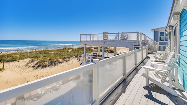 Eine Strandterrasse mit Glasgeländer, Liegestühlen und Blick auf das Meer.