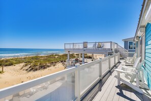 Una terraza frente al mar con barandilla de vidrio, sillas de playa y vista al océano.