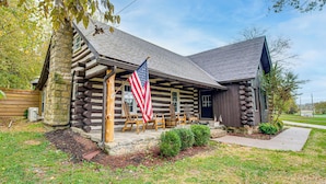 Uma cabana de toras com varanda, bandeira americana e chaminé de pedra.