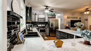 A modern kitchen with stainless steel appliances, a large island, and a ceiling fan. - 1/2 Mi to Sapelo River: Family Home w/ Large Yard (Shellman Bluff)