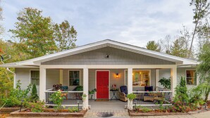A single-story house with a porch, a red door, and a small garden area with potted plants. - Ski Asheville! Mountain-View Hideaway w/ Deck (Asheville)